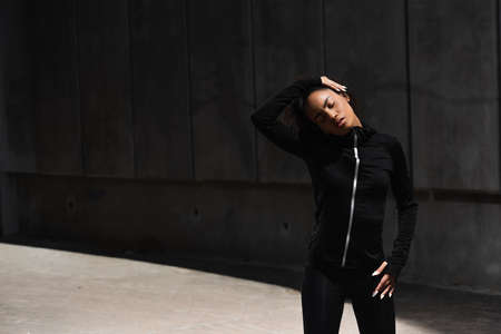 Young african american sportswoman with closed eyes stretching neck outdoorsの写真素材
