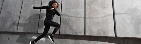 African american sportswoman running near building outdoors, banner
