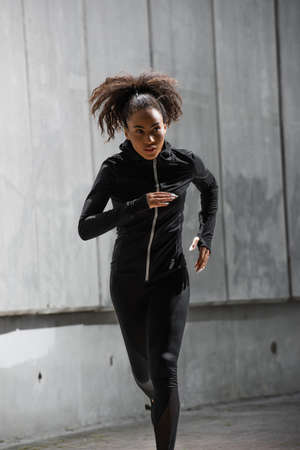 African american runner in black sports jacket looking away while running outdoorsの写真素材