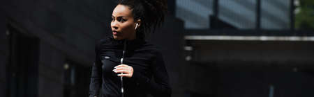African american woman in earphone jogging outdoors, banner