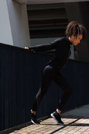 Side view of fit african american sportswoman in earphone warming up near bridgeの写真素材