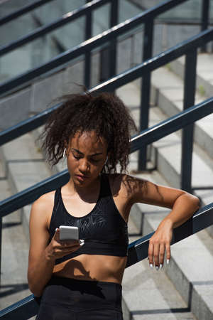 African american sportswoman in earphones using smartphone outdoorsの写真素材