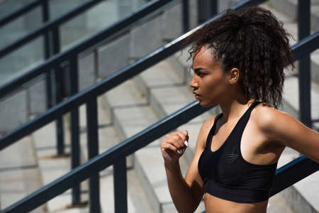 Side view of african american sportswoman in black top looking away on stairs
