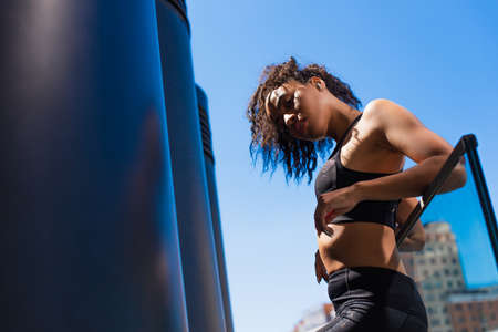 Low angle view of young african american sportswoman in top and wireless earphone looking at camera...