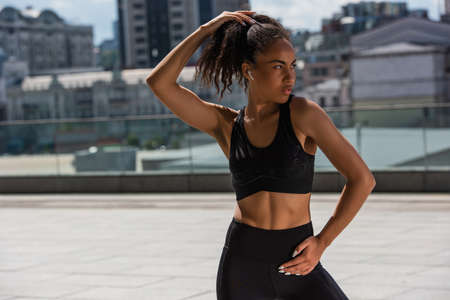 Young african american sportswoman in earphone looking away on urban street