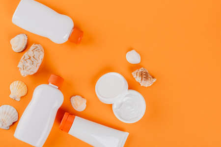 top view of containers with sunblock near cosmetic cream and seashells on orange