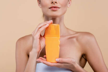 partial view of young woman showing orange bottle of sunblock isolated on beigeの写真素材