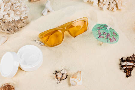 top view of cosmetic cream near orange sunglasses and seashells on sandの写真素材