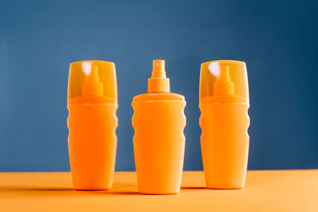spray bottles of sunblock on orange surface isolated on blueの写真素材