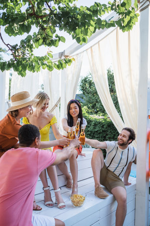 Young people toasting with beer near potato chips in patioの写真素材