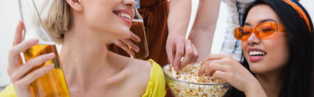 happy multiethnic friends eating popcorn during beer party, bannerの写真素材