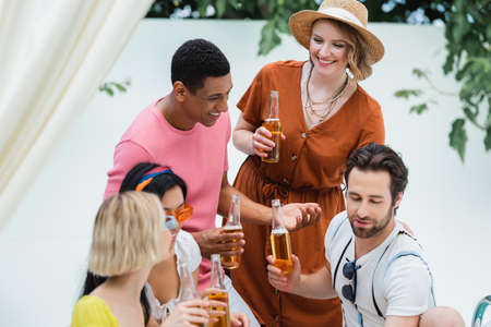 pleased multicultural friends drinking beer during summer party outdoors