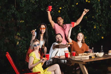 Young interracial friends looking at camera near pizza and beer outdoorsの写真素材