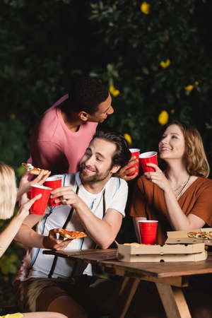 Multiethnic friends with pizza and plastic cups talking during party