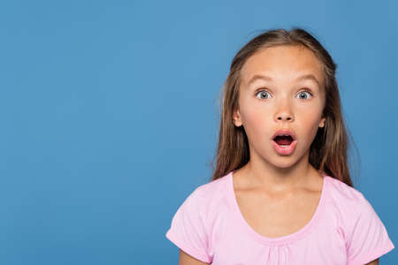 Astonished girl in pink t-shirt looking at camera isolated on blueの写真素材