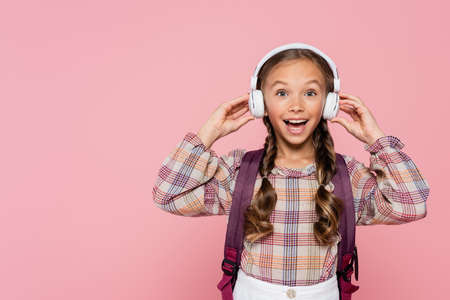 Excited girl with backpack holding headphones isolated on pinkの写真素材
