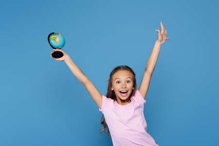 Excited schoolkid holding globe and looking at camera isolated on blue