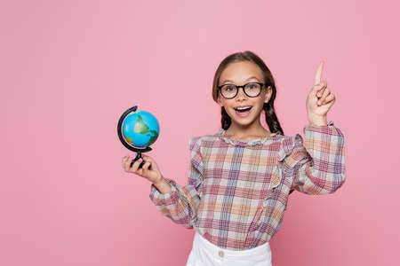 amazed girl with small globe showing idea gesture while looking at camera isolated on pinkの写真素材