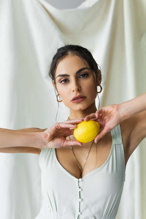 brunette woman in dress holding fresh lemon on white