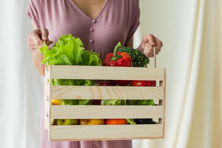 cropped view of woman holding wooden box with vegetables on whiteの写真素材