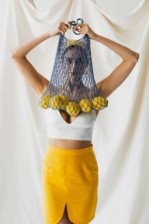 woman in crop top holding string bag with lemons on whiteの写真素材