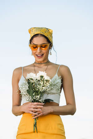 amazed woman in sunglasses and yellow headscarf looking at flowersの写真素材