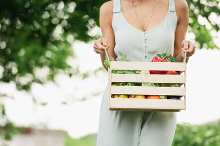 cropped woman holding wooden box with cropped vegetablesの写真素材