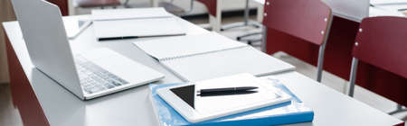 digital tablet and laptop near notebooks on desk in modern school, banner