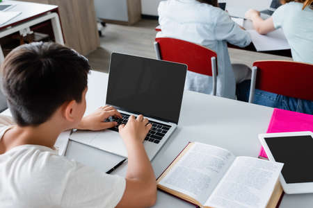Overhead view of schoolboy using laptop with blank screen near bookの写真素材