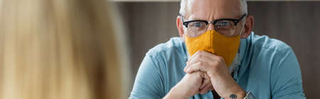 Mature teacher in protective mask looking at blurred pupil, banner