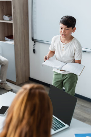 Asian schoolboy with pen and notebook talking in classroomの写真素材