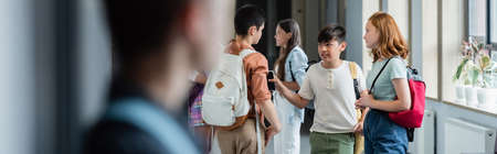 blurred boy standing alone near teenagers talking in school corridor, banner