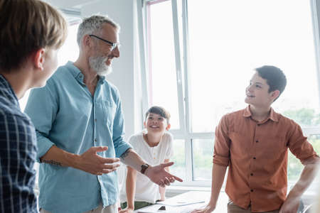 smiling teacher gesturing while talking to multiethnic pupils in classroomの写真素材