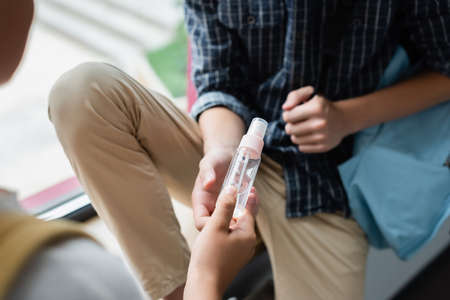 cropped view of schoolboy giving hand antiseptic to friend at schoolの写真素材