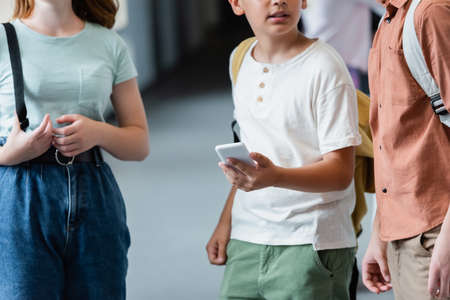 cropped view of schoolboy with mobile phone near classmates