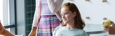 redhead girl smiling near classmates in school dining room, banner