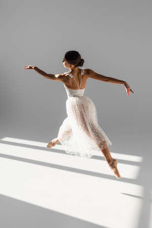 Side view of elegant ballerina jumping in sunlight on gray backgroundの写真素材