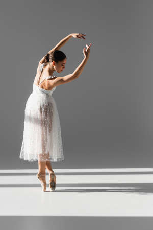 Side view of ballerina bending and looking down on gray background with sunlightの写真素材