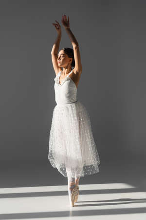 Ballerina dancing with closed eyes on gray background