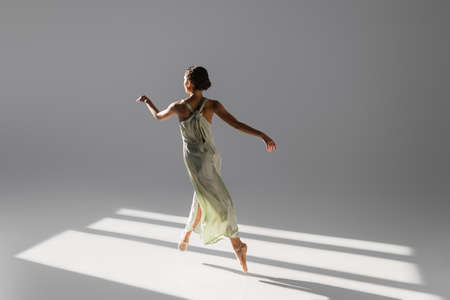 Elegant ballerina dancing and jumping on gray background with sunlightの写真素材