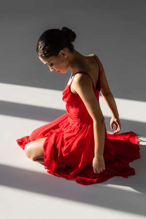 Side view of brunette ballerina in red dress sitting in light on gray backgroundの写真素材