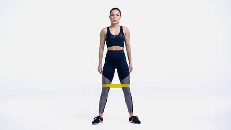 brunette young sportswoman working out with yellow elastics on white