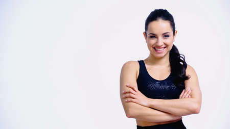 happy young woman in sportswear standing with crossed arms and looking at camera isolated on white