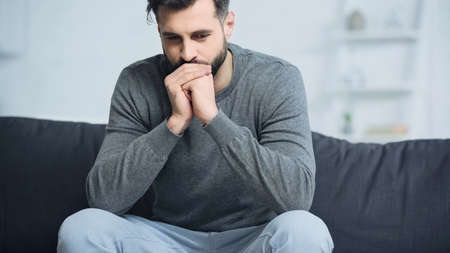 worried man in gray sweater sitting with clenched hands on couch