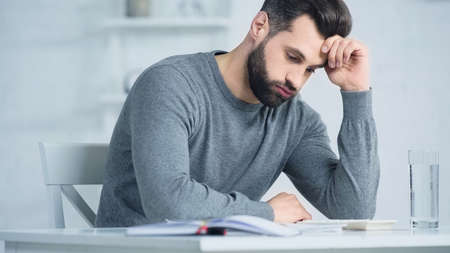 displeased man puffing cheeks and looking at calculator on table