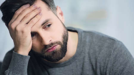 dissatisfied and bearded man touching forehead and looking away