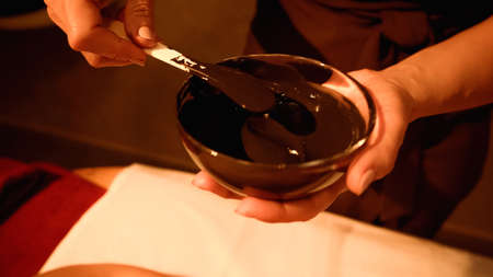 cropped view of beautician mixing mud in bowl with spatulaの写真素材