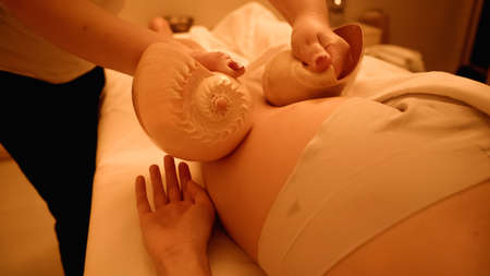 partial view of therapist massaging leg of young woman with sea shells in wellness centerの写真素材