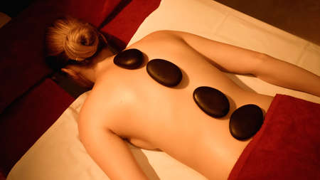 back view of woman receiving hot stone massage in spa salonの写真素材