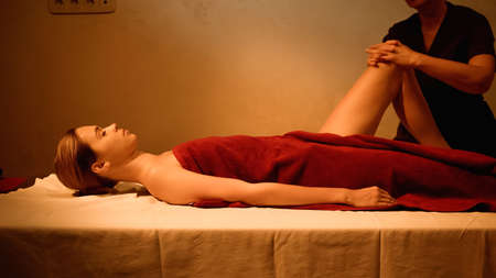 side view of young woman receiving leg massage from professional masseur